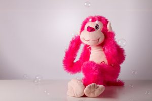 Plush pink monkey plugging its ears with bubbles floating by