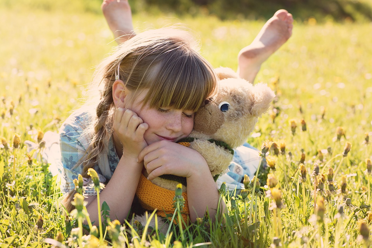 Happy child hugging teddy bear in field of chamomile and dandelions